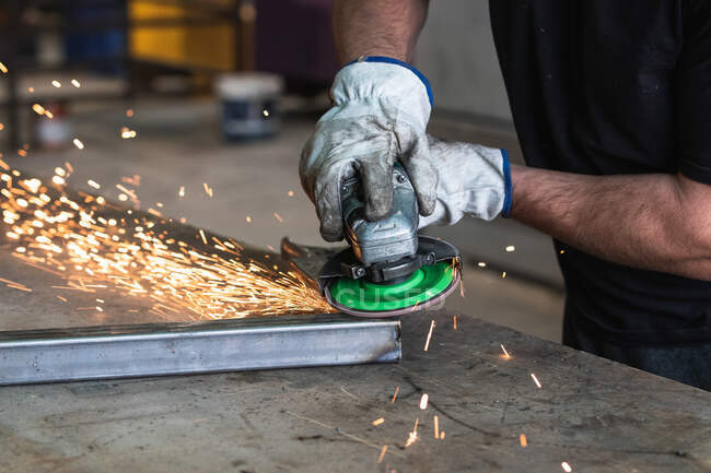 Cropped unrecognizable male welder in protective hardhat using electric grinder and cutting metal detail in grungy workshop — Stock Photo