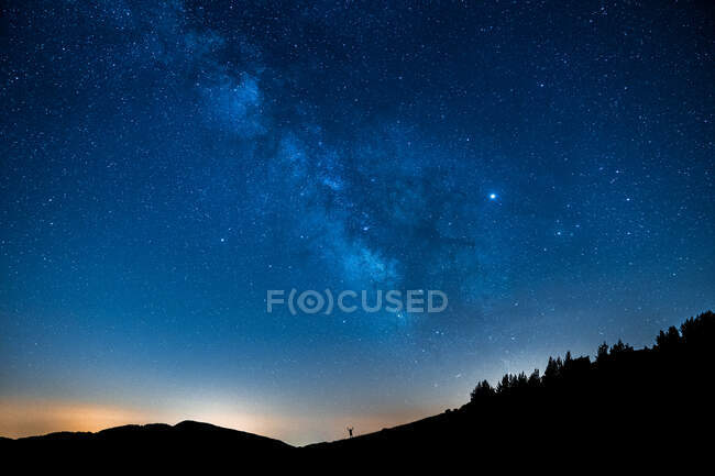 Мальовничий вид на зоряне блакитне небо з хмарами над горою з невизначеними силуетами людини на заході сонця — стокове фото