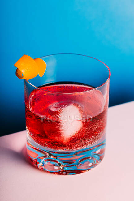 Bicchiere di cocktail alcolico amaro Negroni servito con ghiaccio e buccia d'arancia su superficie chiara — Foto stock