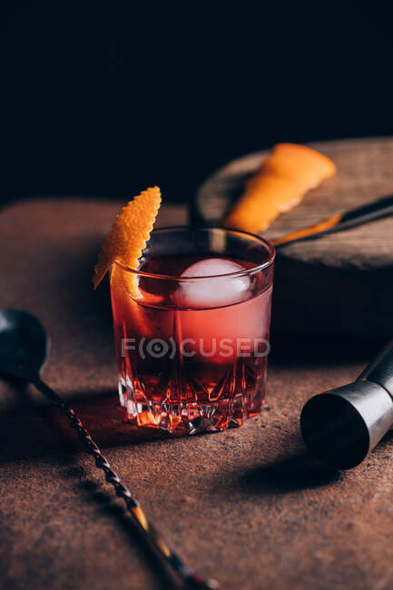 Glass of refreshing alcoholic Negroni cocktail garnished with orange peel and placed on table amidst barman tools — Stock Photo