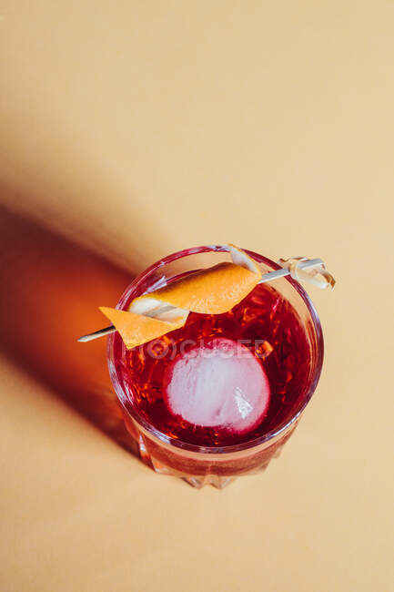Glass of bitter alcoholic Negroni cocktail served with ice and orange peel on light surface — Stock Photo