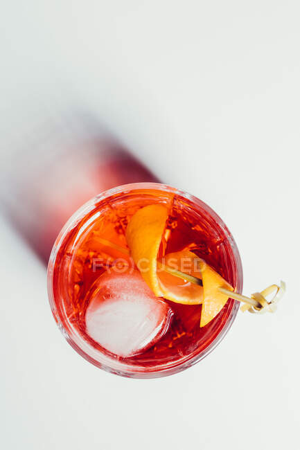 Glass of bitter alcoholic Negroni cocktail served with ice and orange peel on white surface — Stock Photo