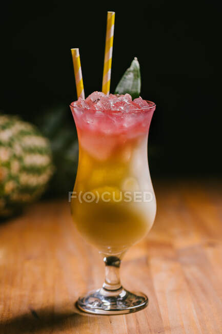 Ein Glas erfrischend süßer Pina Colada Cocktail, garniert mit grünen Blättern, serviert auf einem Holztisch im dunklen Raum — Stockfoto
