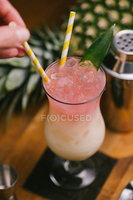 De cima da colheita pessoa sem rosto mexendo com palha delicioso refrescante coquetel Pina Colada servido na mesa — Fotografia de Stock
