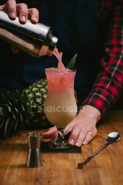 Crop anonymous barman in checkered shirt pouring alcoholic Pina Colada from shaker into glass at bar counter — Stock Photo
