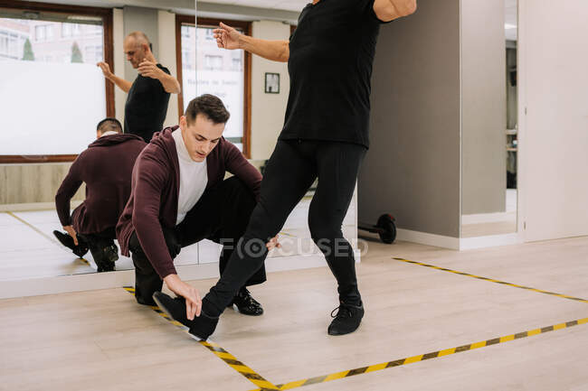 Junger männlicher Instruktor hilft reiferen Tänzern bei Standardtanzbewegungen während des Unterrichts im Saal mit Spiegel — Stockfoto