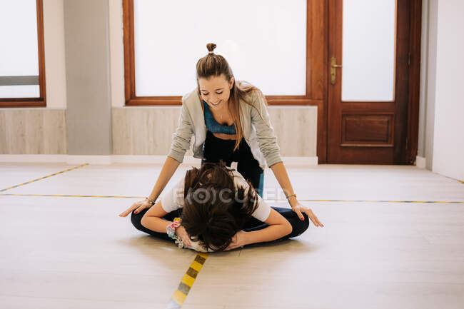 Instrutora feminina alegre ajudando menina flexível com pernas esticadas antes de dançar em estúdio — Fotografia de Stock