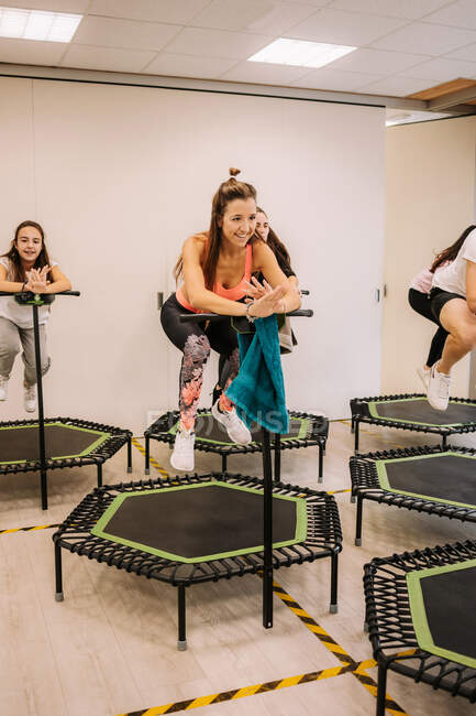 Companhia de atletas que saltam ativamente acima do solo no trampolim ao fazer exercícios durante o exercício de aptidão ativa no ginásio moderno brilhante — Fotografia de Stock
