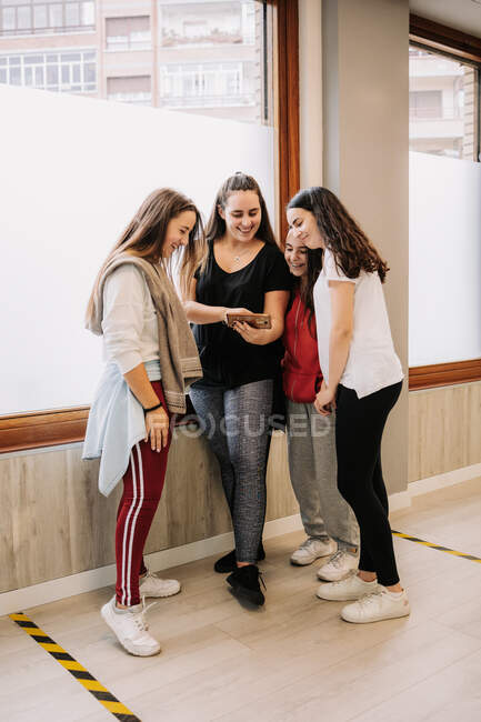 Alto ángulo de jóvenes bailarinas sonrientes que se reúnen en la sala y ven el video de la danza en el teléfono inteligente después de la lección - foto de stock