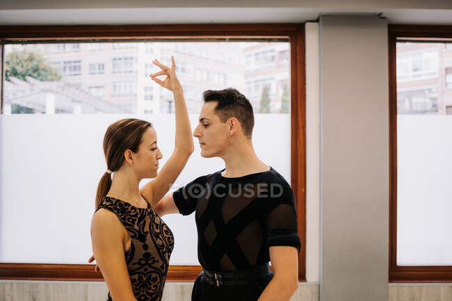 Slender graceful couple performing ballroom dance while rehearsing in bright studio and holding hands — Stock Photo