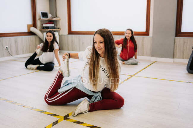 Гнучкі танцюристи-жіночі танцівниці, що сидять в розколах і розтягують ноги, готуючись до уроку в просторому залі — стокове фото