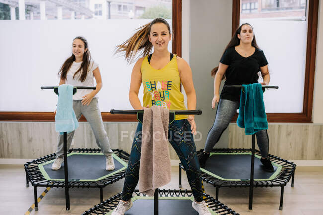 Company of sportspeople jumping on trampolines with raised arms during active fitness training in gym — Stock Photo
