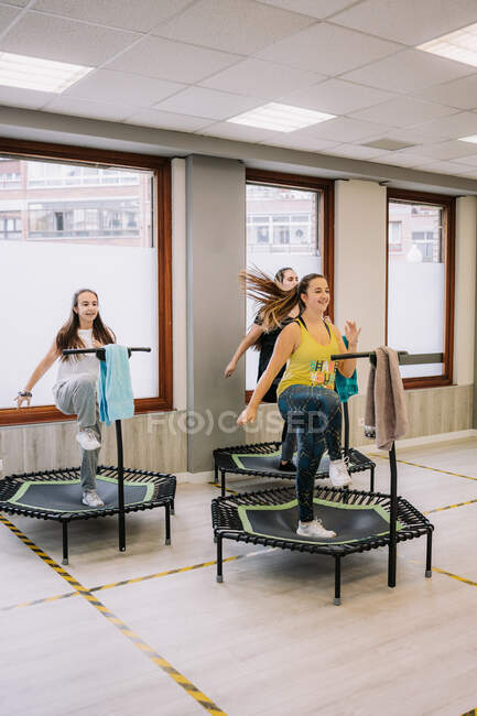 Gesellschaft von Sportlern, die mit erhobenen Armen beim aktiven Fitnesstraining in der Turnhalle auf Trampolinen springen — Stockfoto