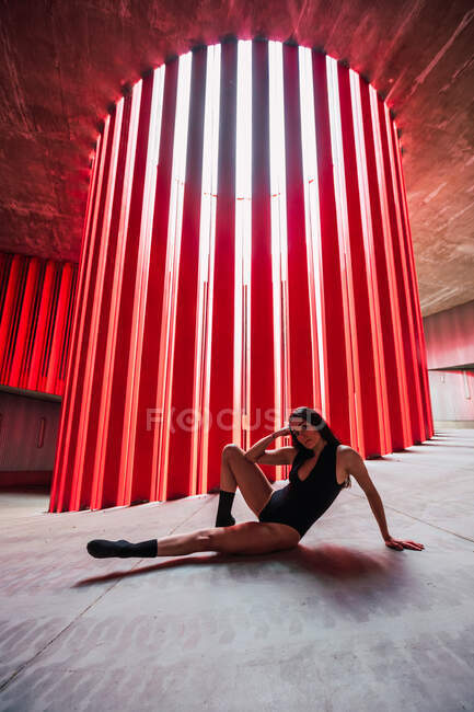 Artista di teatro etnico seduto sul pavimento vicino alla parete luminosa a costine sul palco e guardando la fotocamera — Foto stock