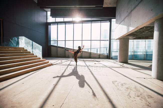 Seitenansicht einer unkenntlichen Theaterkünstlerin, die mit erhobenem Bein und Arm auf dem Boden tanzt und Schatten gegen Glaswand wirft — Stockfoto