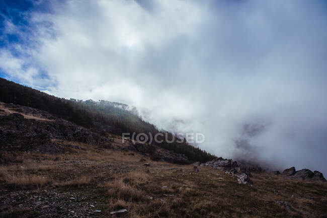 Vista pitoresca de cumes altos com neblina sob o céu azul brilhante com nuvens na luz solar — Fotografia de Stock