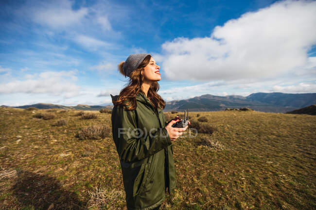 Joven turista femenina con labios pucheros controlando UAV con mando a distancia mientras mira hacia otro lado en el césped en Europa - foto de stock