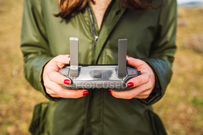 Cropped unrecognizable female tourist with red manicure controlling UAV with remote controller — Stock Photo
