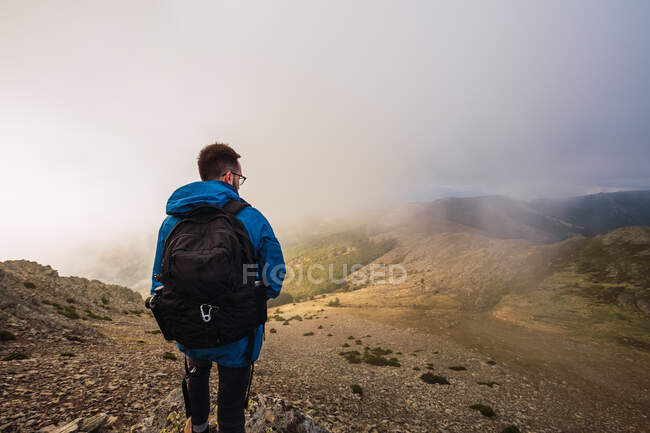 Back view of anonymous male trekker with rucksack standing on pathway against mount on misty day — Stock Photo