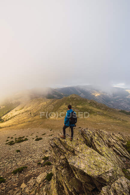 Vue de dessus vers l'arrière du randonneur masculin anonyme avec sac à dos debout sur le chemin contre le mont le jour brumeux — Photo de stock