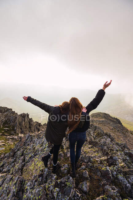 Vue arrière de voyageuses anonymes qui contemplent le mont lors d'un voyage sous un ciel nuageux en Europe — Photo de stock