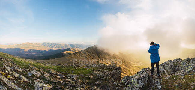 From above back view of anonymous male traveler with backpack taking photo of mount on camera on foggy day — Stock Photo