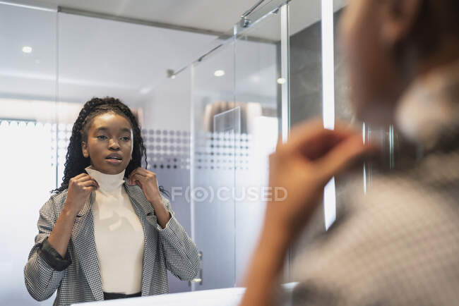 Visão traseira da colheita auto-assegurada feliz jovem preto feminino millennial na roupa da moda sorrindo e tocando roupas enquanto olha no espelho no banheiro — Fotografia de Stock