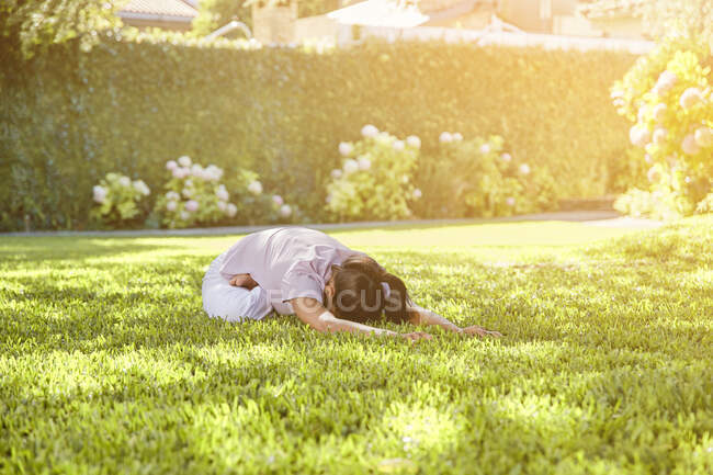 Donna flessibile irriconoscibile in abiti sportivi dimostrando posa bambino durante la pratica dello yoga sul tappeto in giardino — Foto stock