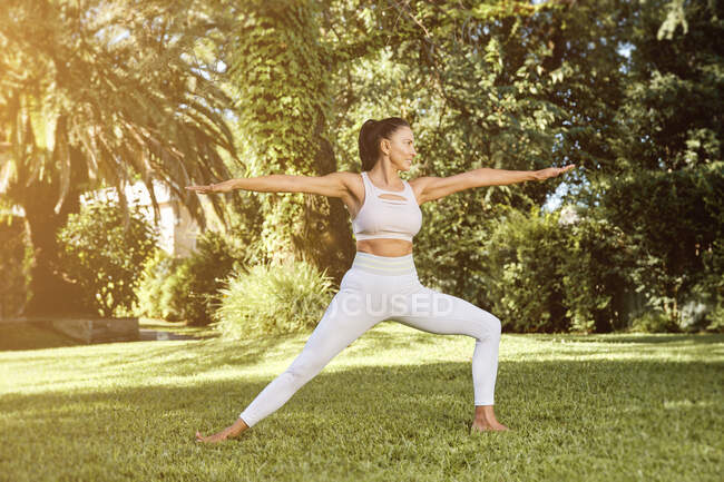 Side view of happy flexible female in sports clothes demonstrating Virabhadrasana two pose while practicing yoga on mat and looking away — Stock Photo