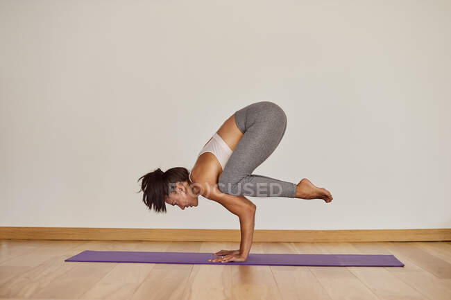 Side view of strong female in sportswear standing in Bakasana pose on floor in studio room — Stock Photo