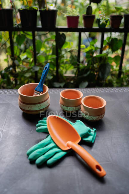 Сверху коллекция садовых инструментов и керамических горшков для пересадки растений, поставленных на стол в теплице — стоковое фото