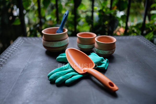Сверху коллекция садовых инструментов и керамических горшков для пересадки растений, поставленных на стол в теплице — стоковое фото
