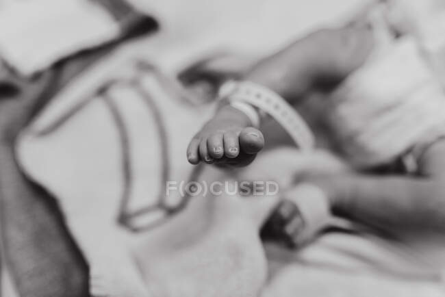 Foco suave preto e branco da colheita bebê recém-nascido irreconhecível em fralda com etiqueta na perna deitada no berço do hospital — Fotografia de Stock