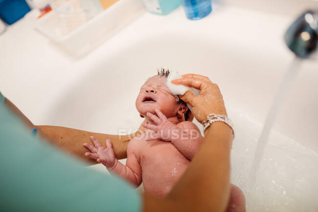 Alto ángulo de cultivo enfermera anónima con esponja de algodón que da baño para el niño pequeño recién nacido en el hospital - foto de stock