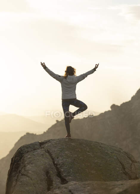 Rückansicht einer nicht wiedererkennbaren Frau, die auf dem Gipfel eines felsigen Berges steht und bei Sonnenuntergang Tree with Arms Up posiert — Stockfoto