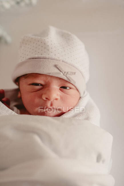 Primer plano lindo dulce pequeño recién nacido niño en sombrero blanco envuelto en manta durante los primeros días de vida - foto de stock