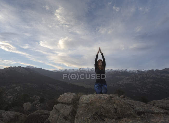 Ruhige Frau mit geschlossenen Augen bei Yoga-Übungen während sie Meditation auf Thunderbolt Pose auf felsigem Boden bei hellem Sonnenuntergang praktiziert — Stockfoto
