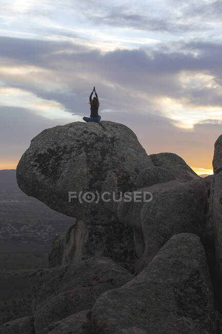 Back view of unrecognizable calm female performing yoga exercise while practicing mediation on rocky ground at bright sunset — Stock Photo