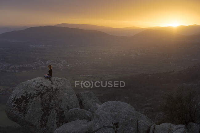 Сверху вид спокойной женщины, выполняющей упражнения йоги, практикующей медиацию на каменистой земле на ярком закате — стоковое фото