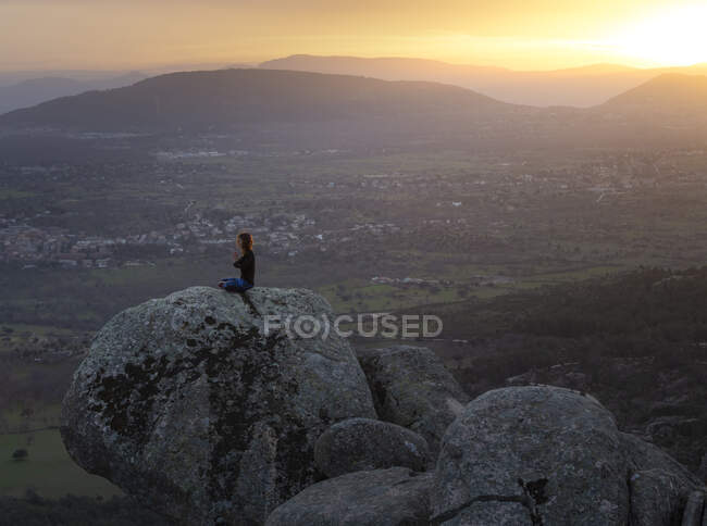 From above side view of calm female performing yoga exercise while practicing mediation on rocky ground at bright sunset — Stock Photo