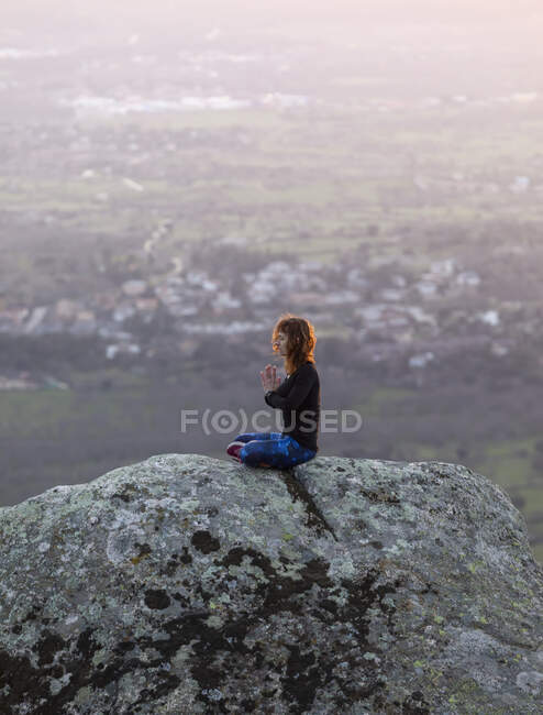 From above side view of calm female performing yoga exercise while practicing mediation on rocky ground at bright sunset — Stock Photo
