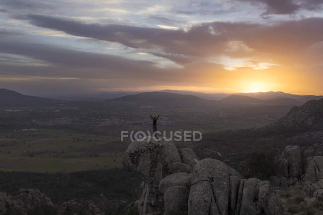 Visão traseira da fêmea irreconhecível em pé no topo da montanha rochosa e fazendo pose de montanha durante o pôr do sol — Fotografia de Stock