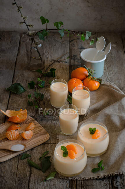 Alto ángulo de sabrosa mousse de mandarina adornado con hojas de menta fresca servida en copas de vidrio sobre mesa de madera - foto de stock