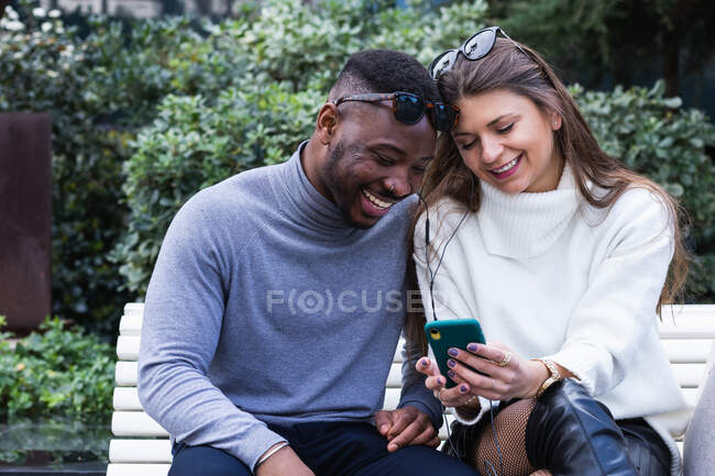 Crop vista di contenuti per adulti coppia multirazziale innamorata ascoltare musica sul telefono cellulare, mentre trascorrere del tempo insieme nel parco — Foto stock