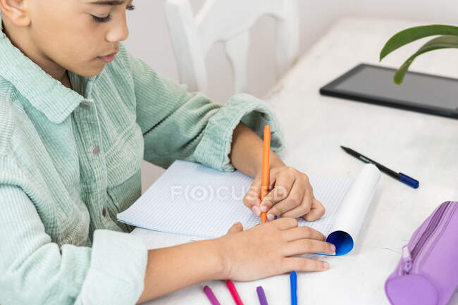 Desde arriba vista lateral de la cosecha escolar negro tomando notas en el cuaderno mientras estudia en la mesa en casa - foto de stock