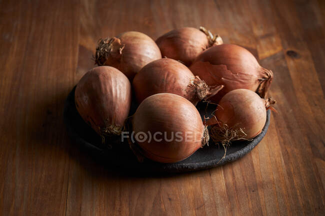 Alto ángulo de racimo de cebollas frescas sin pelar colocadas en la placa sobre la mesa de madera - foto de stock