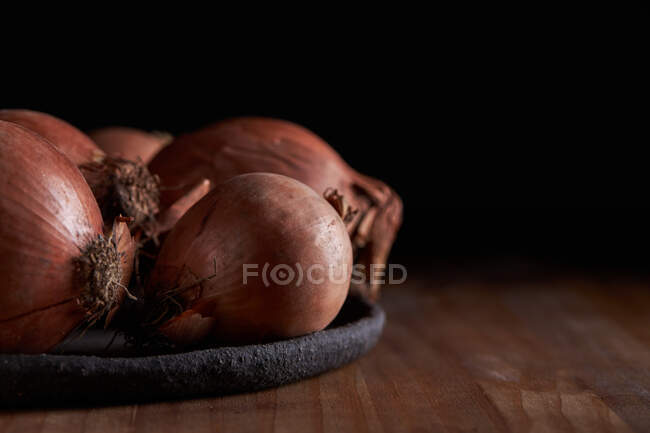Куча свежего неочищенного лука на тарелке на деревянном столе — стоковое фото