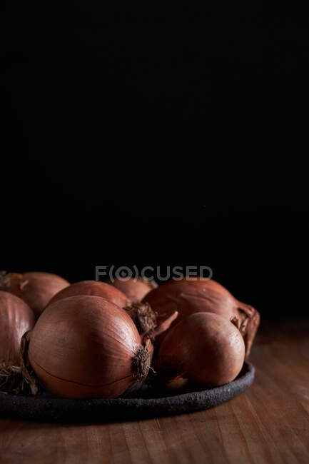 Куча свежего неочищенного лука на тарелке на деревянном столе — стоковое фото