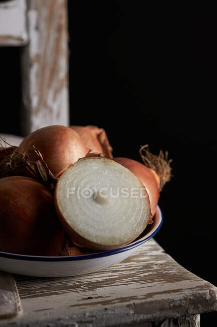 Closeup halved and whole unpeeled onions placed in bowl on shabby chair on black background — Stock Photo