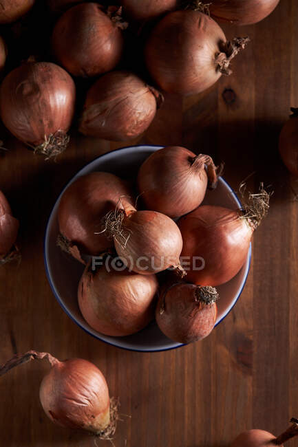 Ângulo alto de molho de cebolas frescas não descascadas colocadas na placa na mesa de madeira — Fotografia de Stock